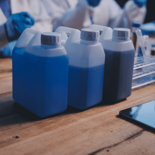 Galões de produtos químicos de cores azuladas em uma mesa de madeira